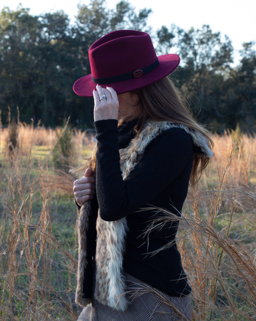 Person wearing a purple hat and fur vest standing in a field