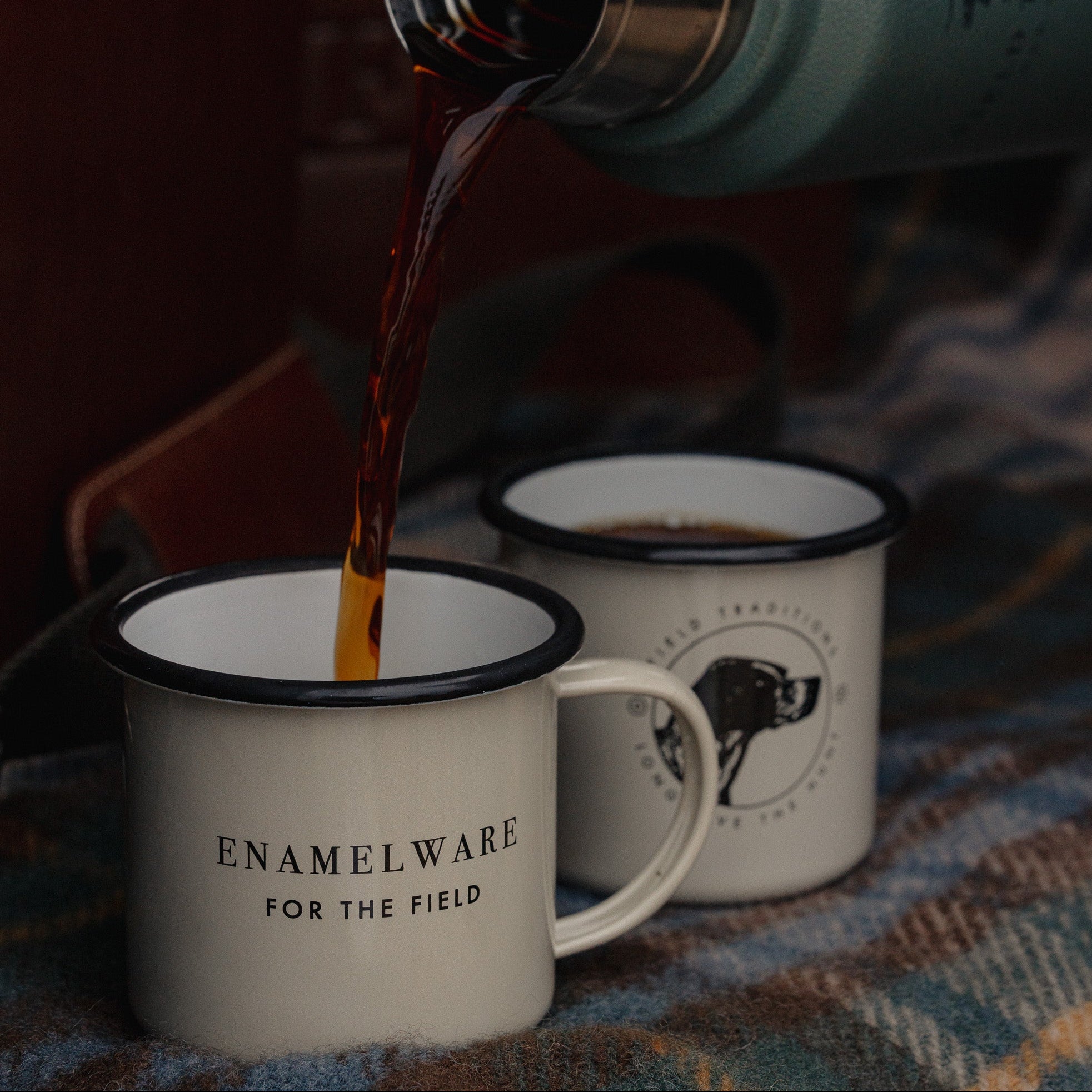 Enamelware mug being filled with coffee on a patterned fabric background